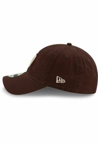 Casquette de baseball marron avec un bord incurvé, texture en tissu, détail brodé du logo sur le devant, et petit emblème sur le côté.