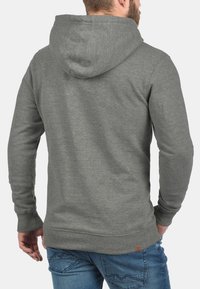 Grå hættetrøje med snøre, med et enkelt design og en ribbet kant. Båret med blå jeans, der fremviser en afslappet stil.