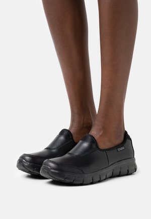 Black slip-on shoes made of smooth leather with elastic accents and a textured rubber sole. Designed for comfort and ease of wear.