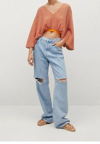 Haut court à motifs rouges et orange avec un décolleté en V profond, associé à un jean taille haute déchiré bleu clair et des sandales plates beige.