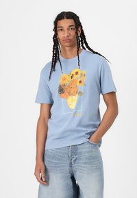 Světle modré bavlněné tričko s grafikou slunečnic ve váze, orámované světle zelenou barvou, s textem "van Gogh" v žluté.