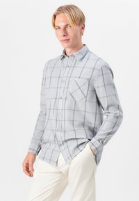 Camisa de manga larga de cuadros grises con un bolsillo en el pecho, cierre frontal con botones y una textura de tela suave. Presenta un cuello clásico y un dobladillo recto.