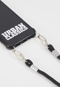 Fekete telefon tok, az "URBAN CLASSICS" logóval, fém klipszekkel és fekete fonott pántokkal felszerelve, a biztonságos hordozás érdekében.