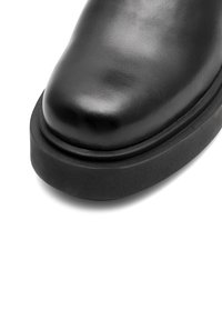 Melnas ādas zābaks ar noapaļotu purngalu un biezu gumijas zoli. Gluda textūra bez redzamām rakstām un rotājumiem.