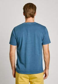 T-shirt κοντομάνικο σε μεσαίο μπλε βαμβάκι, με στρογγυλή λαιμόκοψη, απαλό ύφασμα και χαλαρή εφαρμογή; ορατές ραφές κατά μήκος του στριφώματος.