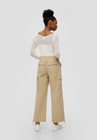 Witte lange mouw top met doorschijnende achterkant, gecombineerd met beige wijdvallende cargo pantalons met een multi-pocket ontwerp en een trekkoord aan de onderkant.