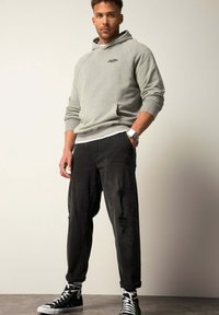 Sudadera con capucha de color gris claro, con un bolsillo en el frente, combinada con jeans negros desgastados. Zapatillas altas negras completan el conjunto.