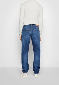 Blå denimjeans med rak beninformation, med bakfickor med dekorativ sömnad och en tag i tanläder på midjan.