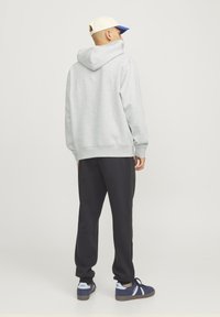 Szary hoodie z kieszonką kangurką, ściągaczami przy mankietach i u dołu, w połączeniu z czarnymi spodniami i sneakersami z niebieskimi akcentami. Czapka ma niebieski daszek.