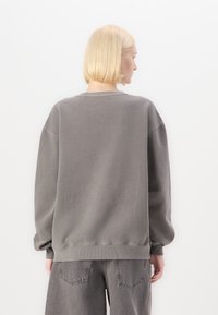 Felpa grigia oversize con maniche lunghe e polsini a costine, realizzata in un tessuto morbido. Il retro presenta un design semplice e un colletto a girocollo.