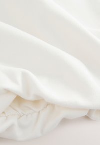Tissu en coton blanc avec une texture lisse, présentant des bords froncés et des détails de couture subtils. Apparence douce et légère.