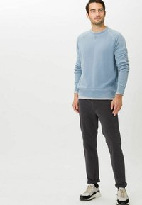 Blauw katoenen sweatshirt met lange mouwen en geribbelde manchetten, gecombineerd met donkergrijze broek. Het model draagt sneakers met lichte accenten.