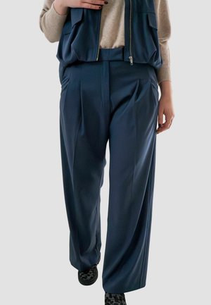 Navyblauwe wijde broek van soepel materiaal met voorplooien. Gedragen met een gelaagde vest, met twee voorzakken en een rits.
