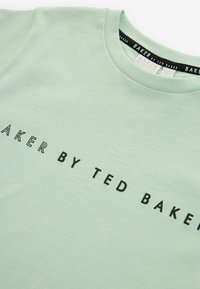 Camiseta verde claro hecha de una tela suave, con texto negro "BAKER BY TED BAKER" impreso horizontalmente en la parte delantera.