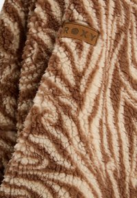 Bruine en crème fuzzy fleece stof met een zebra-printpatroon; bevat een leren label met de tekst "ROXY" geïntegreerd in het ontwerp.