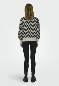 Maglione lavorato a maglia con motivo zigzag bianco e nero, dal taglio rilassato e maniche a palloncino, abbinato a jeans skinny neri e stivali chunky.