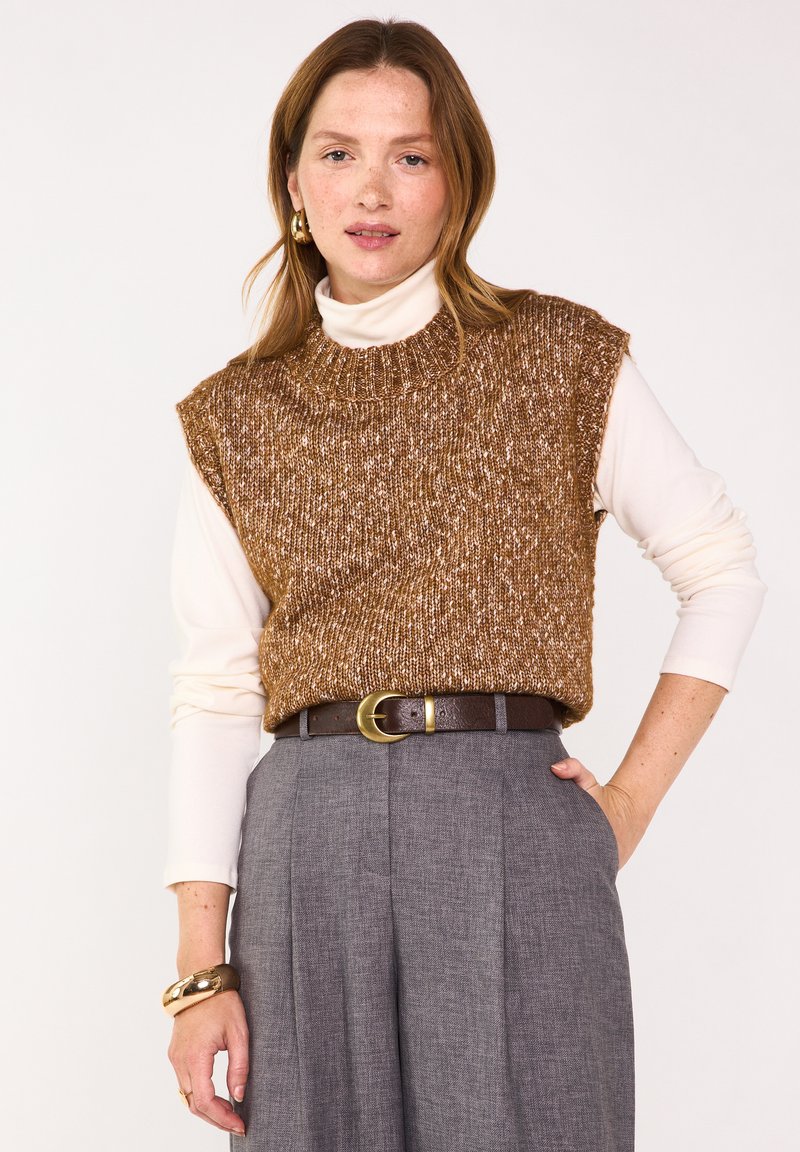 Gilet lavorato a maglia marrone con scollo rotondo sopra un dolcevita bianco. Abbinato a pantaloni grigi plissettati e una cintura marrone con dettagli in oro.