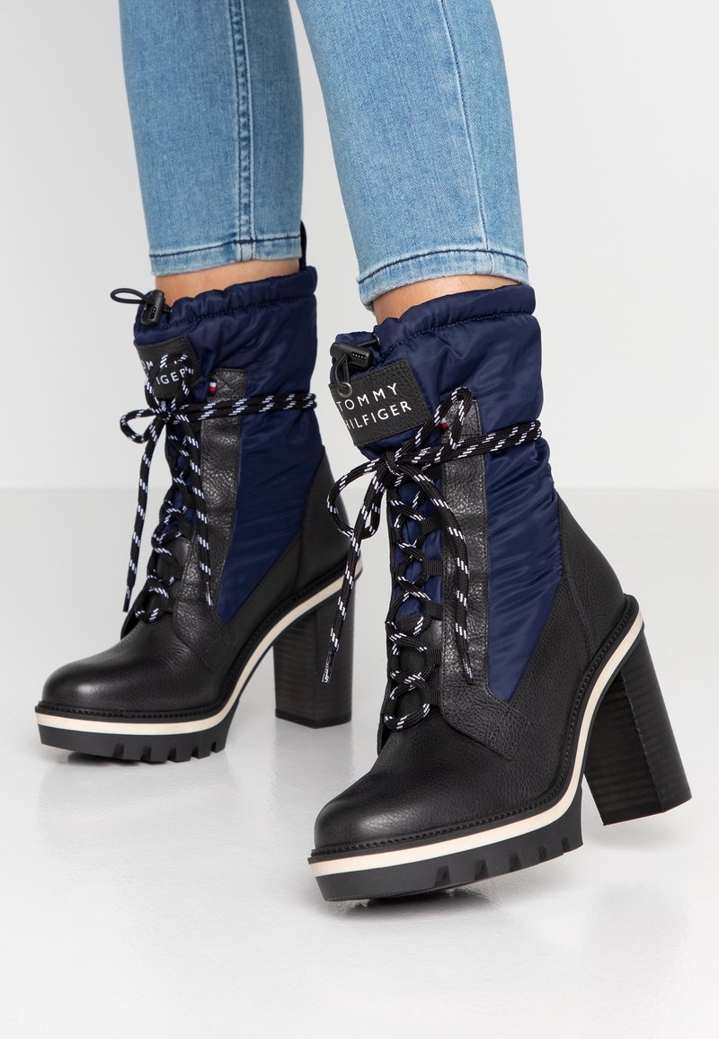 Bottes à lacets montantes à talons hauts en cuir noir et matelassé marine, portées avec un jean bleu clair.