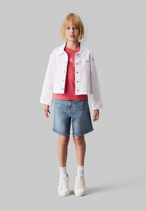 Chaqueta de mezclilla blanca, camiseta roja con logo, pantalones cortos de mezclilla azules, zapatillas blancas y calcetines blancos hasta el tobillo. Un conjunto sencillo y casual.