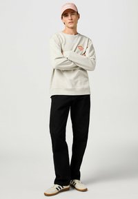 Sudadera gris claro con texto rojo, pantalones negros y zapatillas beige con rayas negras. Atuendo casual con una gorra rosa.