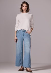 Un suéter de punto gris claro con cuello redondo, combinado con unos vaqueros de mezclilla de pierna ancha en un tono azul claro. El conjunto incluye unos zapatos planos de leopardo en tono marrón.