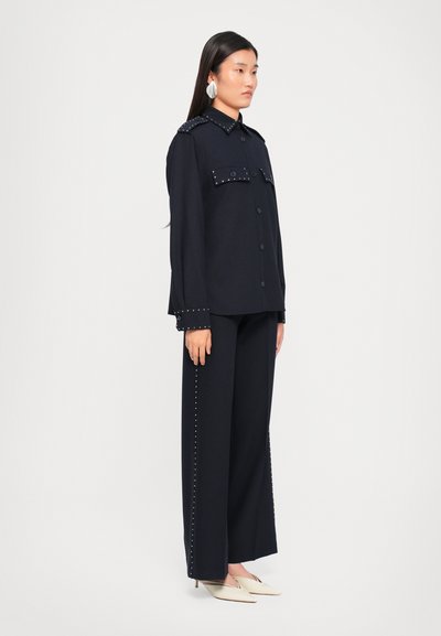 Navy blue oversized button-up shirt with studded collar and cuffs, paired with matching wide-leg trousers adorned with studded side seams.