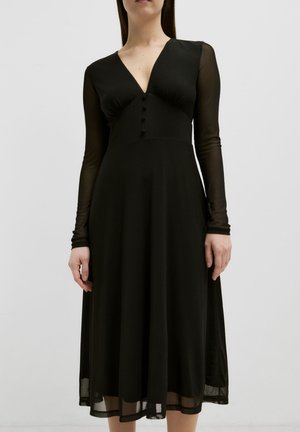 Schwarzes Kleid mit langen, durchsichtigen Ärmeln, V-Ausschnitt und Knopfdetails. Fließende Silhouette mit einem knielangen Saum und leichter Textur am Rock.