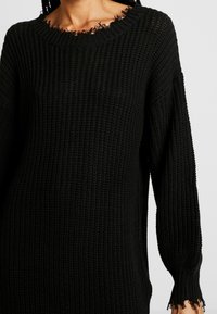 Maglione nero lavorato a maglia con una vestibilità morbida, caratterizzato da una superficie testurizzata, scollo rotondo e bordi sfrangiati al colletto e ai polsini.