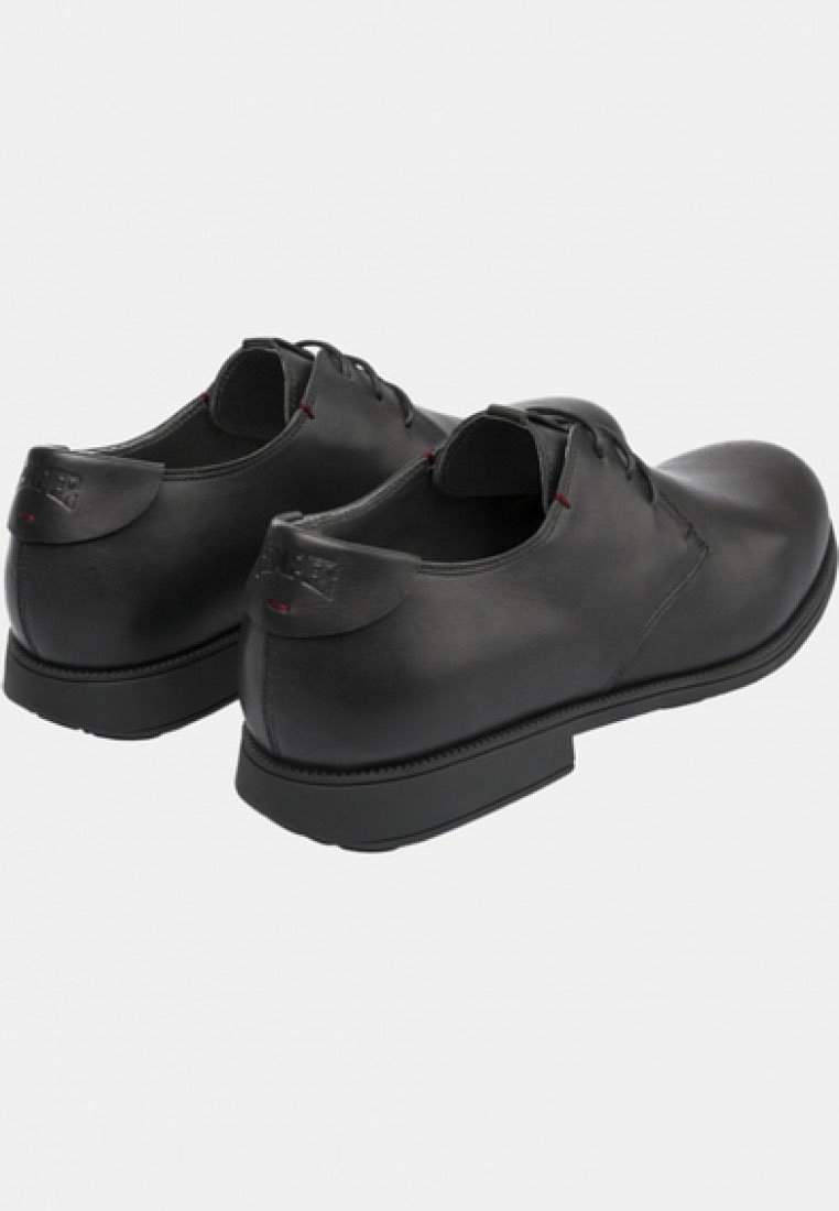 Schwarze Lederschuhe mit runder Zehenform, Schnürdesign, glatter Textur und minimalen Details, ergänzt durch einen kontrastierenden roten Akzent am Kragen.