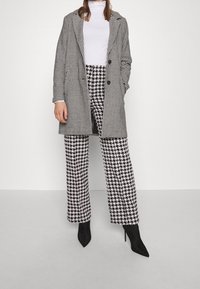 Abrigo de doble botonadura en blanco y negro con estampado de pata de gallo y pantalones de pierna ancha a juego. Combinado con tacones negros puntiagudos, textura suave en todo el conjunto.