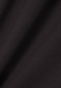 Lähikuva mustasta teksturoidusta kankaasta, jossa näkyy hieno verkkokudonta ja hienovaraiset taitokset, jotka luovat pehmeitä varjoja.