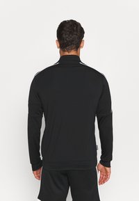 Black athletic jacket with a high collar, long sleeves, and white stripes along the shoulders; smooth texture and fitted design.