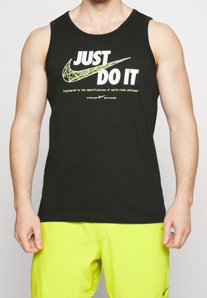 Mann trägt ein schwarzes ärmelloses Shirt mit großem Nike-Logo und dem Schriftzug "Just Do It", kombiniert mit leuchtend gelben Shorts.