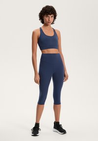 Mornarsko modra aktivna oblačila, ki vključujejo krojeno majico na kratke rokave in legice do kolen. Tkanina je gladka, s prilegajočim krojem in minimalnimi šivi.