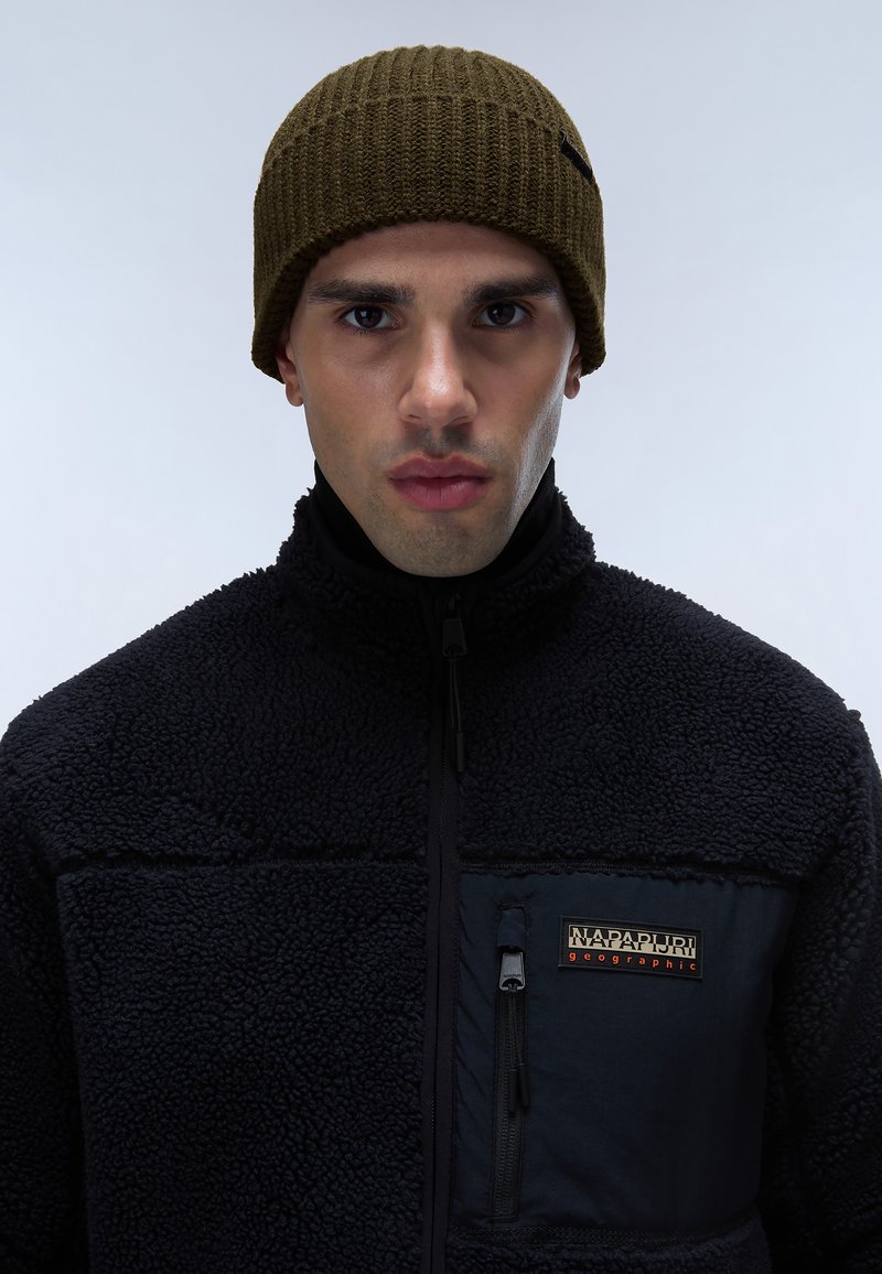 Man med en olivgrön stickad mössa och svart zip-up fleecejacka med Napapijri Geographic-logotyp på bröstfickan.
