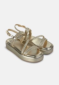 Sandales dorées avec un design de bride tressée, bout ouvert et une semelle épaisse. Équipées d'une bride ajustable à la cheville pour un maintien sécurisé.