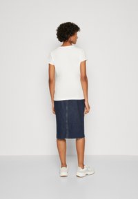 Camiseta blanca de mangas cortas combinada con una falda lápiz de mezclilla, que presenta un corte recto, dobladillo sin terminar y unas zapatillas blancas informales.