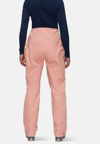 Wasserdichte rosa Skihosen mit hoher Taille und seitlichen Reißverschlusstaschen, kombiniert mit einem dunklen Langarmshirt. Glatte Textur und lockere Passform.