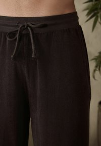 Pantalones de lounge de rizo negros con cintura elástica y cordón, que presentan una textura suave y un ajuste relajado. Sin patrones ni acentos visibles.