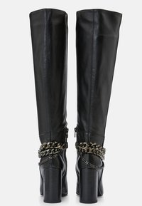 Mustat nahkasaappaat polven yli, joissa on tukevat palikkakorkeudet, hopeiset ketjuyksityiskohdat nilkassa ja sivuvetoketju.