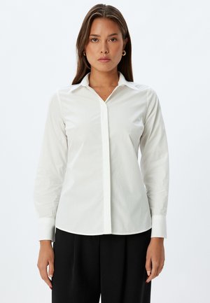 Camicia bianca con maniche lunghe, colletto a punta e tessuto morbido. Presenta un orlo dritto e una pattina anteriore nascosta per un aspetto pulito.