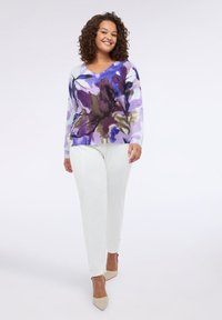 Maglione leggero a maglia con scollo a V in un motivo floreale viola e blu; abbinato a pantaloni bianchi; modello che indossa scarpe a punta color nude.