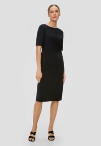 Robe noire midi avec des manches courtes et un col bateau. Tissu léger et lisse avec un détail torsadé au niveau de la taille.