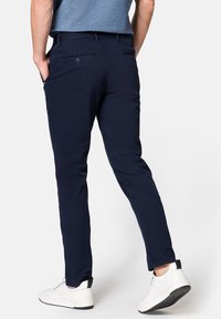 Granatowe chinosy o slim fit, wykonane z gładkiego materiału. Posiadają tylne kieszenie z guzikami oraz podwinięte mankiety, które eksponują białe trampki.