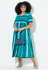 Pasiasta, turkusowa sukienka maxi z krótkimi rękawami, dekoltem w serek i marszczoną talią. Zestawiona z dżinsową torebką i jasno-niebieskimi balerinkami.