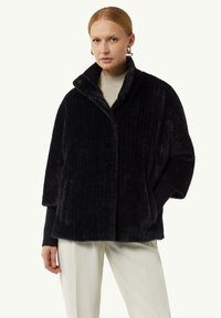 Giacca nera con texture, colletto alto, maniche ampie e tasche frontali. Realizzata in materiale morbido e peloso con un motivo a coste verticali.