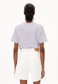 Lilafarbene Baumwoll-T-Shirt mit entspanntem Schnitt und kurzen Ärmeln, kombiniert mit weißen Jeans-Shorts, die ein sichtbares Logopatch am Bund haben.