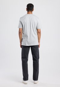 Graues Baumwoll-T-Shirt mit kurzen Ärmeln, Rundhalsausschnitt, gerader Schnitt. Kombiniert mit dunklen Jeans und weißen Turnschuhen, aus der Rückansicht gesehen.