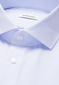 Col de chemise bleu clair avec boutons, présentant un motif texturé subtil et une étiquette de marque "seidensticker" visible à l'intérieur du col.