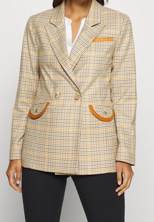Veste à carreaux beige avec des tons jaunes et bruns, poches d'appoint brunes et double boutons. Tissu lisse avec une forme structurée.